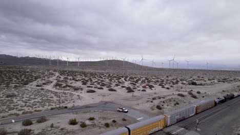 Imágenes-Aéreas-De-Drones-Del-Tren-De-Carga-En-El-Desierto-De-Palm-Springs-Con-Parques-Eólicos-En-El-Fondo,-Tiro-Lento-Hacia-Delante