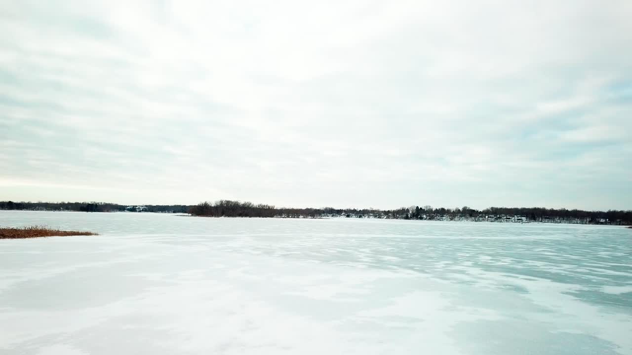 Low fly through trees in the foreground and across a frozen lake in the midwest. 4K