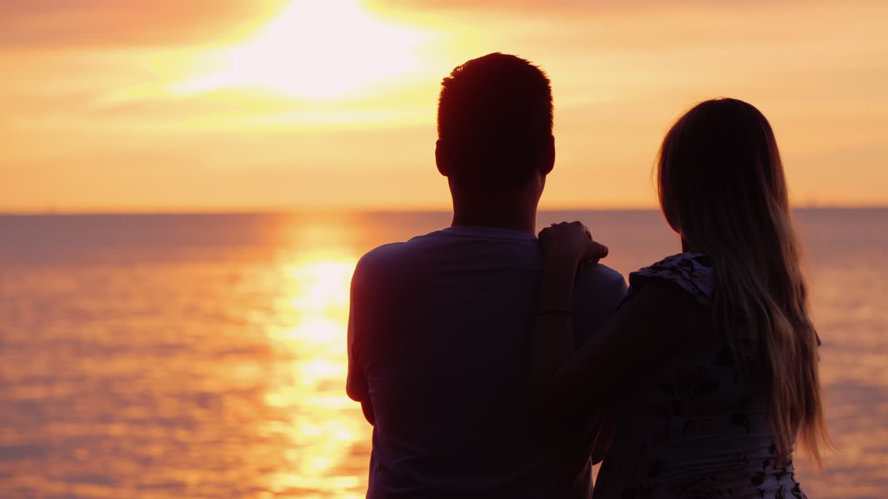 사랑에 빠진 다민족 부부는 바다 위의 일몰을 존경합니다