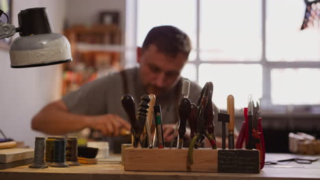 hand of master takes cutter from rack to process leather