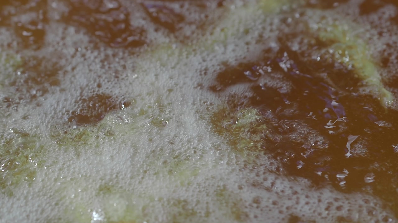 Close-up of Bubbling Liquid with White Foam and Green Particles