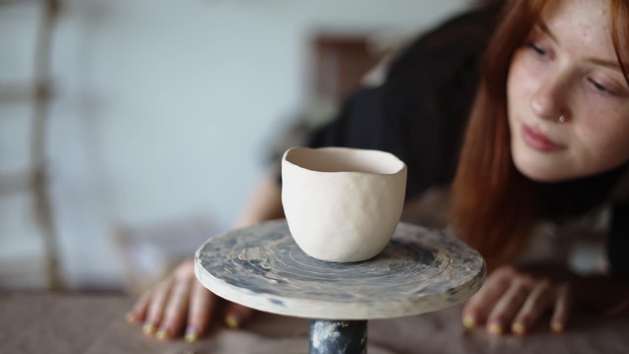 The red-haired girl potter checks her work and spins the potter's wheel