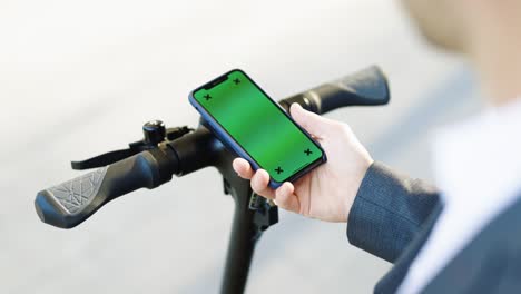 closeup of electric scooter hand with chromakey screen of smartphone. tourist uses phone with green screen rents electric scooter using mobile phone app. eco friendly transportation