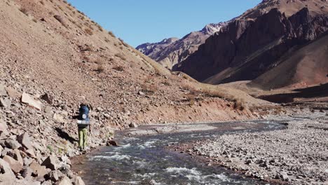 hiker walking along a river in the andes mountains at high altitude. mendoza, argentina.