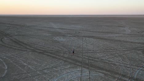 Hombre-Solitario-Parado-En-El-Crepúsculo,-Paisaje-Interminable-De-Salinas-Con-Senderos-Para-Automóviles