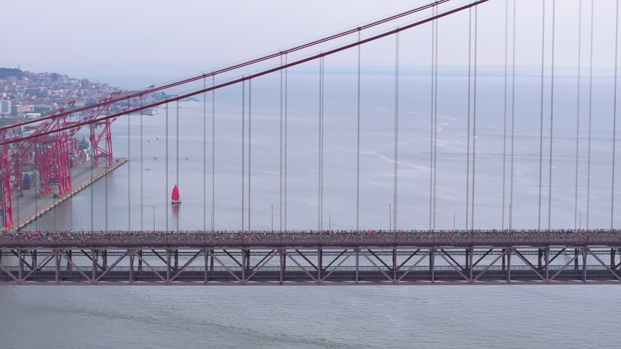 Toma aérea lateral con dron de media maratón y carrera de larga distancia de 10 km en Lisboa, Portugal, Europa. Corredores cruzando el emblemático puente rojo 25 de Abril