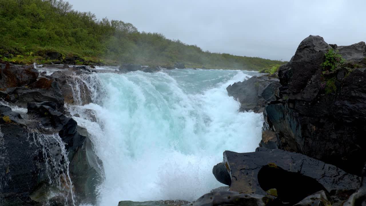 río con una poderosa cascada cerca del bosque y entre las rocas negras