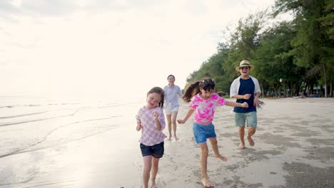 4k asian family parents with two little daughter playing on the beach together at summer sunset.