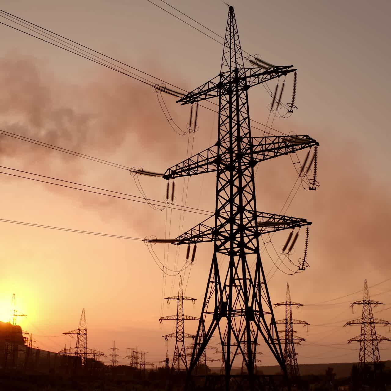 Transmission lines near smoking industrial pipe at sunset. High-voltage electric power line and dark smoke released from factory in the evening