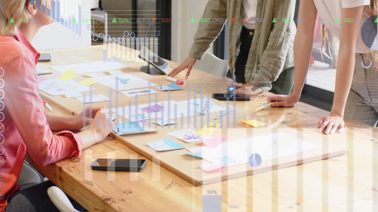 Seated designer reading notes design team moving notes and tapping tablet animating data for review