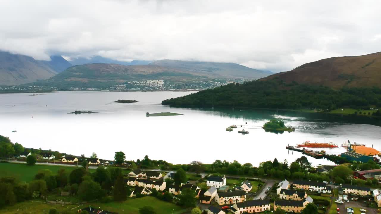 안개 낀 산들을 배경으로 한 스코틀랜드 호숫가 마을의 시네마틱 패닝 드론 샷