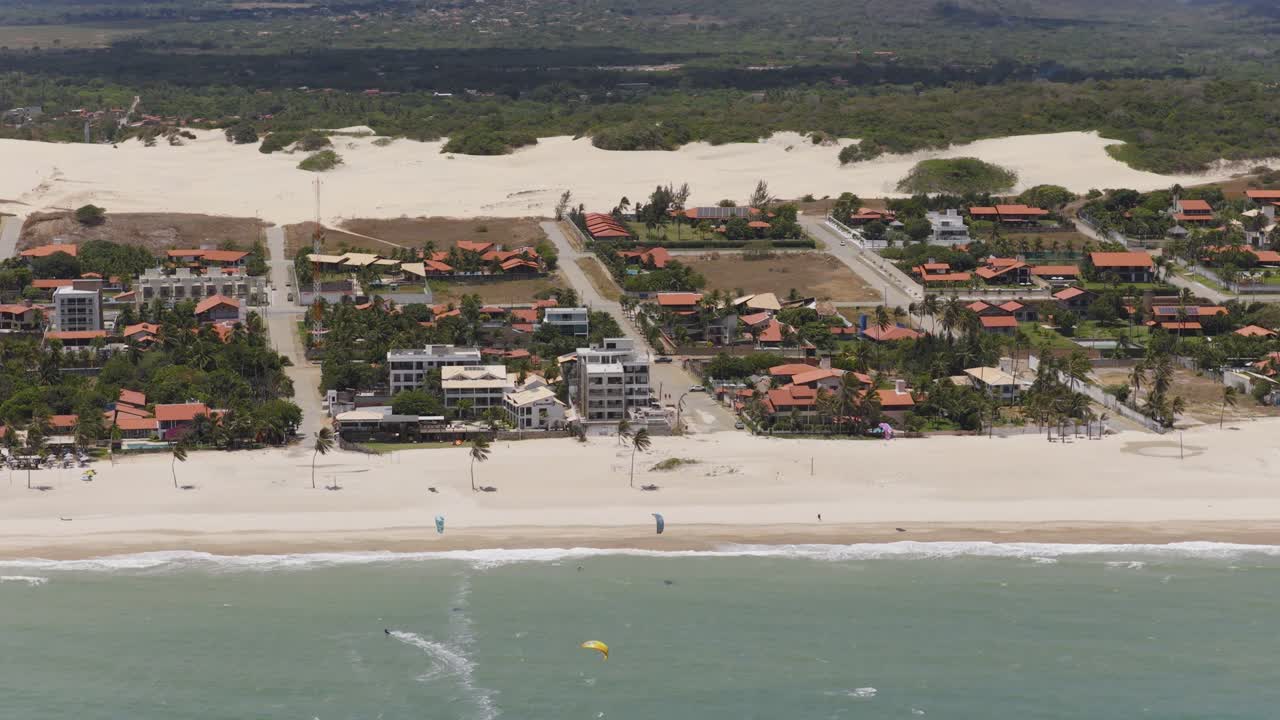 Cumbuco, Caucaia, Ceará, Brasil, com resorts à beira-mar, praia de areia, kitesurfistas ao largo e um extenso campo de dunas no interior, plano de estabelecimento com descida de drone