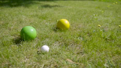 vista de cerca de tres coloridas bolas de petanca en el césped, luego el jugador lanza otra bola cerca