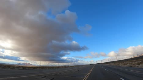 Fahrt-Entlang-Der-Wüstenlandschaft-In-Der-Abend--Oder-Morgendämmerung-Mit-Windkraftanlagen-Am-Horizont---Fahrersicht