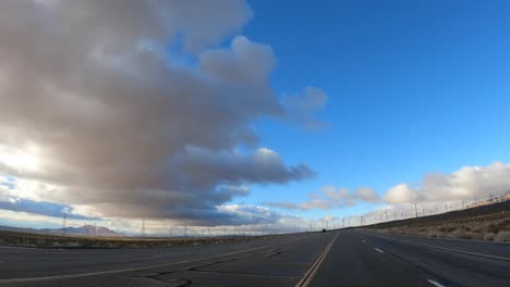 conduciendo a lo largo del paisaje desértico al atardecer o al amanecer con turbinas eólicas en el horizonte - punto de vista del conductor