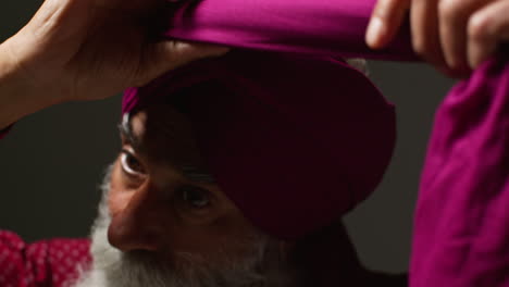 close up low key studio lighting shot of senior sikh man with beard tying fabric for turban against dark background 3