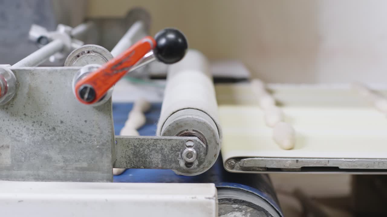 Fresh Bread Dough Rolls  Moving On Conveyor Belt And Being Pressed By Roller. Low Angle, Slow Motion