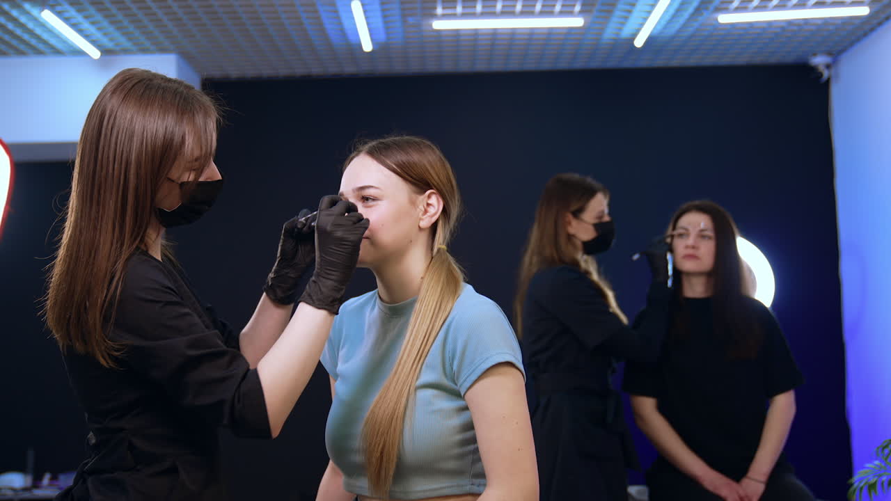Beauticians in masks working with clients in salon. Women having cosmetology procedures on eyebrows. Permanent eyebrow make up.