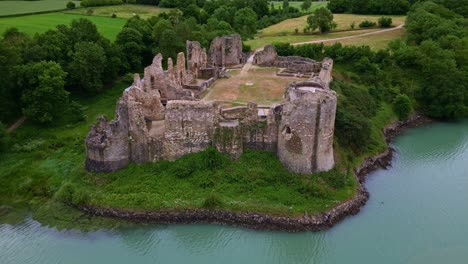 drone moves closer while descending toward the guildo castle ruins, revealing the estuary, vegetation, stone walls and inner courtyard in brittany, france
