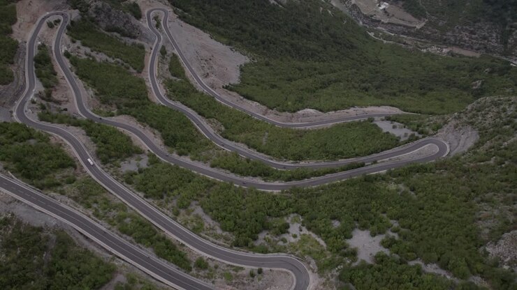 Drone video of descriptive panning over the "Rrapsh Serpentine" mountain pass on the Sh20 road in Grabom,Albania, you can see a motorcycle and car passing by