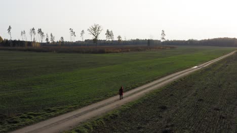 Slow-pan-of-lonely-red-coat-girl-walking-towards-bright-sunlight-and-forest