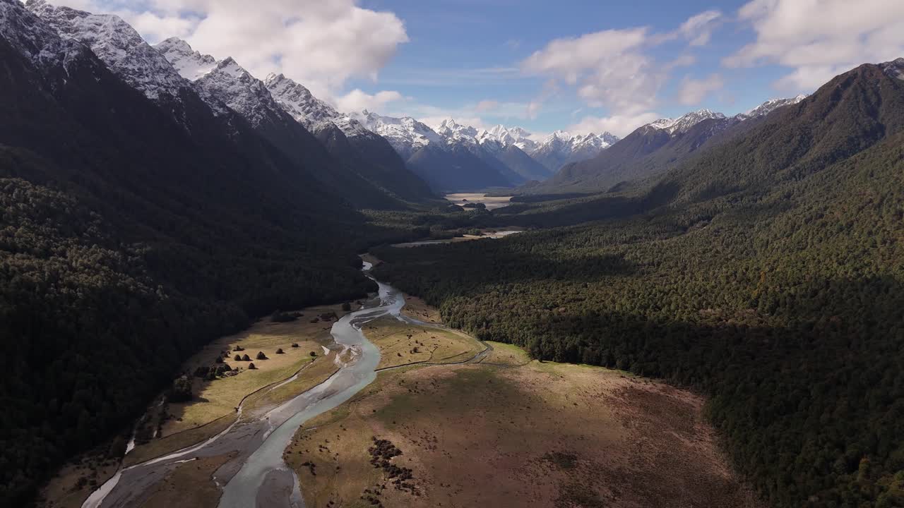 Filmato aereo cinematografico di un limpido torrente di montagna che scorre tra le cime innevate nel Southland, Nuova Zelanda, ripreso lungo la strada panoramica per Milford Sound