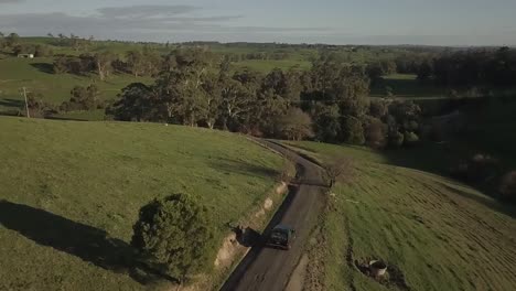 vintage 4wd suv drives slowly along gravel road surrounded by grassy green pasture
