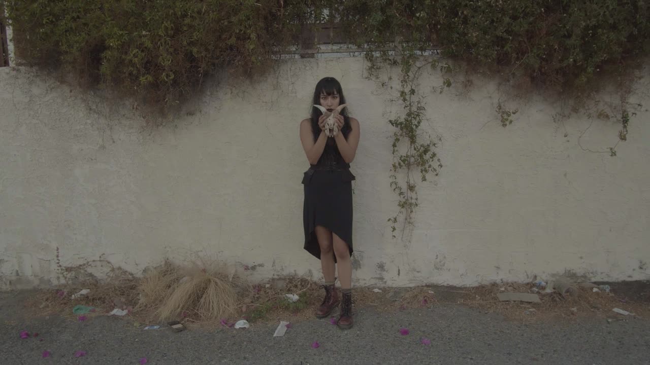 Zoom out of scary girl with long black hair, showing the skull of an animal with horns.