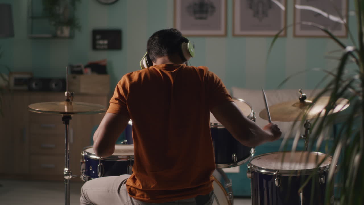 Rear View of Male Musician Playing Drums in Studio Talented Rock Drummer Rehearsing alone in Night Rear View of Male Musician Playing Drums in Studio Talented Rock Drummer Rehearsing alone in Night with Man Enjoying Music and Rhythm Express your Emotions Feelings and Talent