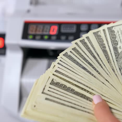woman holding money near counting machine at table indoors, closeup