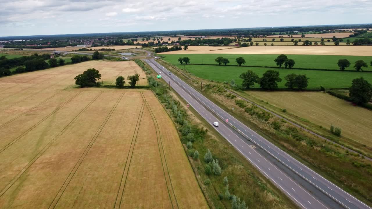 Norfolk dual carriageway through country fields just outside Norwich. The Broadland Northway with a small amount of vehicles travelling along during the day captured by aerial footage