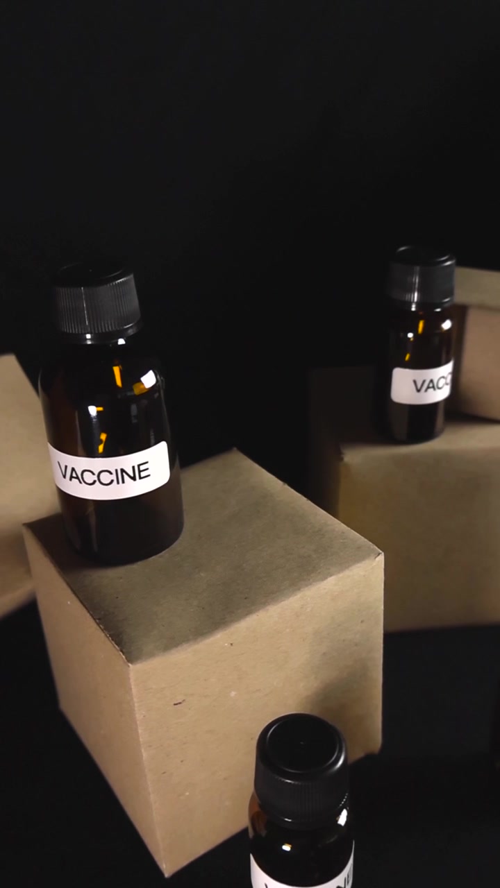 Camera gliding through a dark scene with several cardboard boxes and glass vials labeled as a vaccine, representing the complex logistics, shipping, and distribution of medical supplies