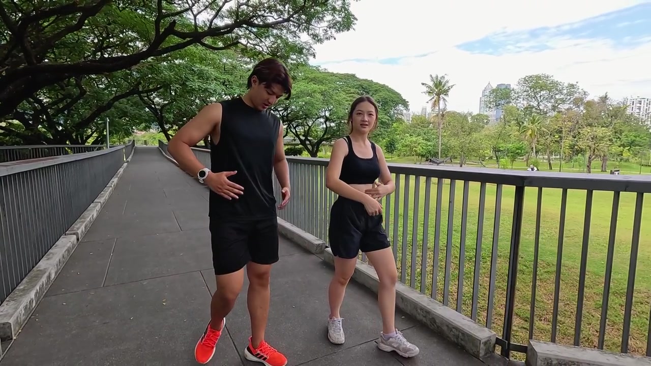 Pasangan Asia yang aktif berjalan melintasi jembatan taman mengenakan pakaian olahraga hitam selama rutinitas olahraga siang hari.