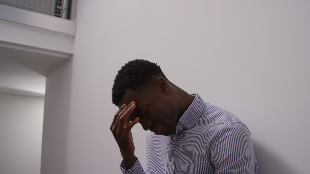 Young Man With Mental Health Issues Standing Leaning Against Wall In Office Looking Depressed And Unhappy Shot In Real Time
