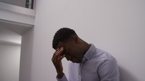 young man with mental health issues standing leaning against wall in office looking depressed and unhappy shot in real time