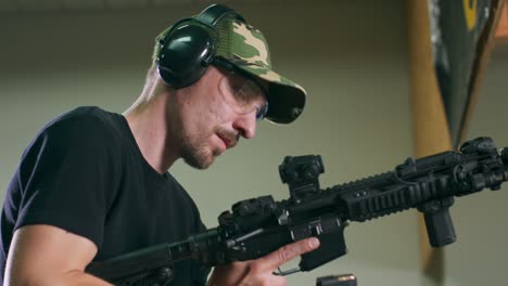 a man loads a magazine clip onto a rifle and fires a round at an indoor firing range