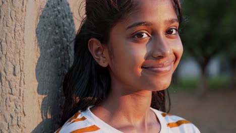 young girl leaning against tree trunk, basking in golden hour sunlight, expressing peaceful contentment with gentle smile radiating natural beauty and tranquil mood