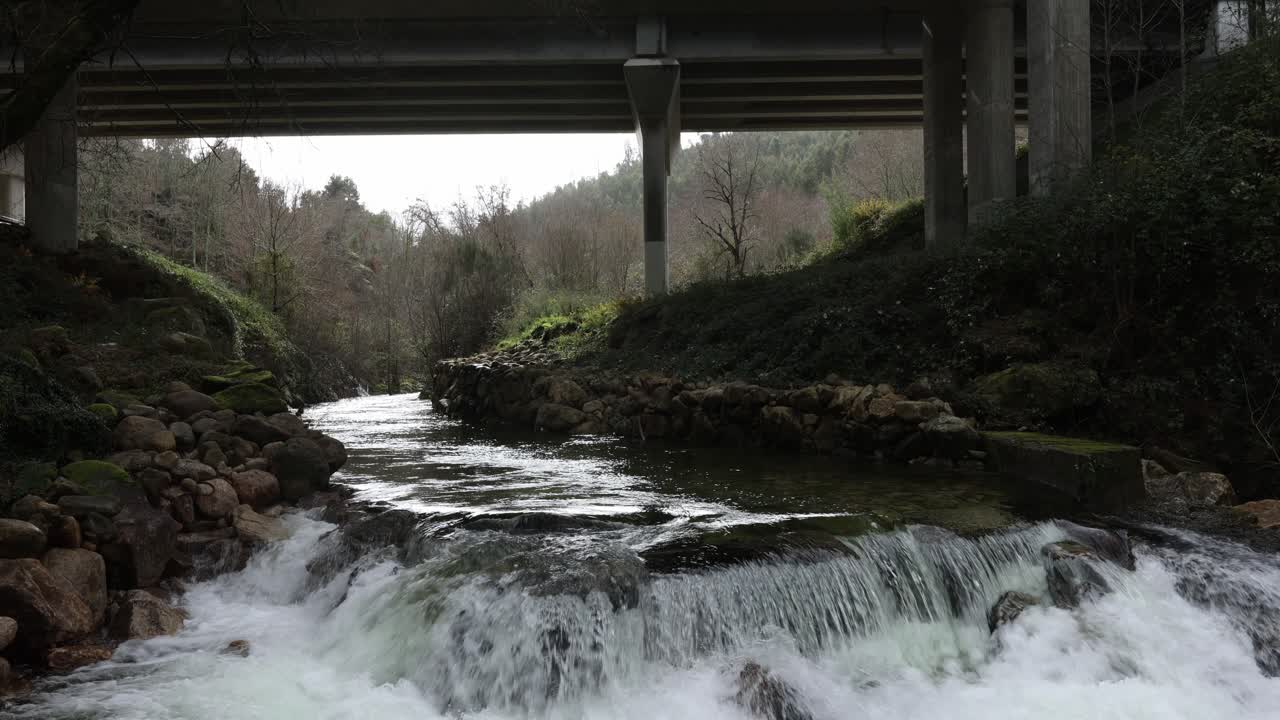 Cascata fluviale sotto un viadotto stradale.