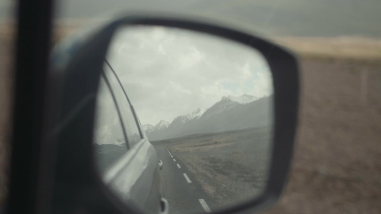 Strada panoramica e montagne riflesse nello specchietto retrovisore dell'auto