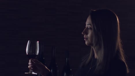 mujer morena girando una copa de vino tinto en una sala de estudio romántica de ambiente oscuro, cámara lenta
