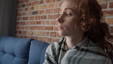 zoom in video of depressed young caucasian woman covered with blanket  and sitting on sofa