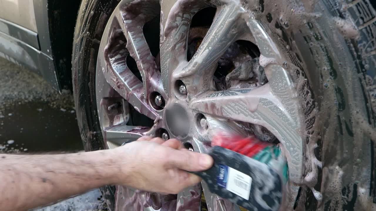 Close up of cleaning SUV alloy wheel faces with red and green bristle wheel brush slow motion