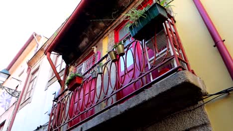 Unique-view-of-a-tiny-street-of-Porto-with-vibrant-red-doors-on-a-balcony,-panning-left