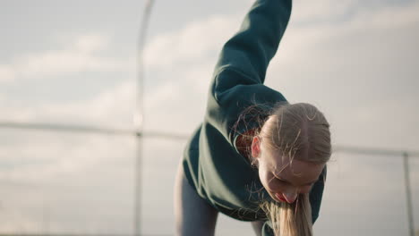 young lady in green sweater bending forward in fitness routine as her hair flutters in wind, showing energy and movement with a clear outdoor setting in the background