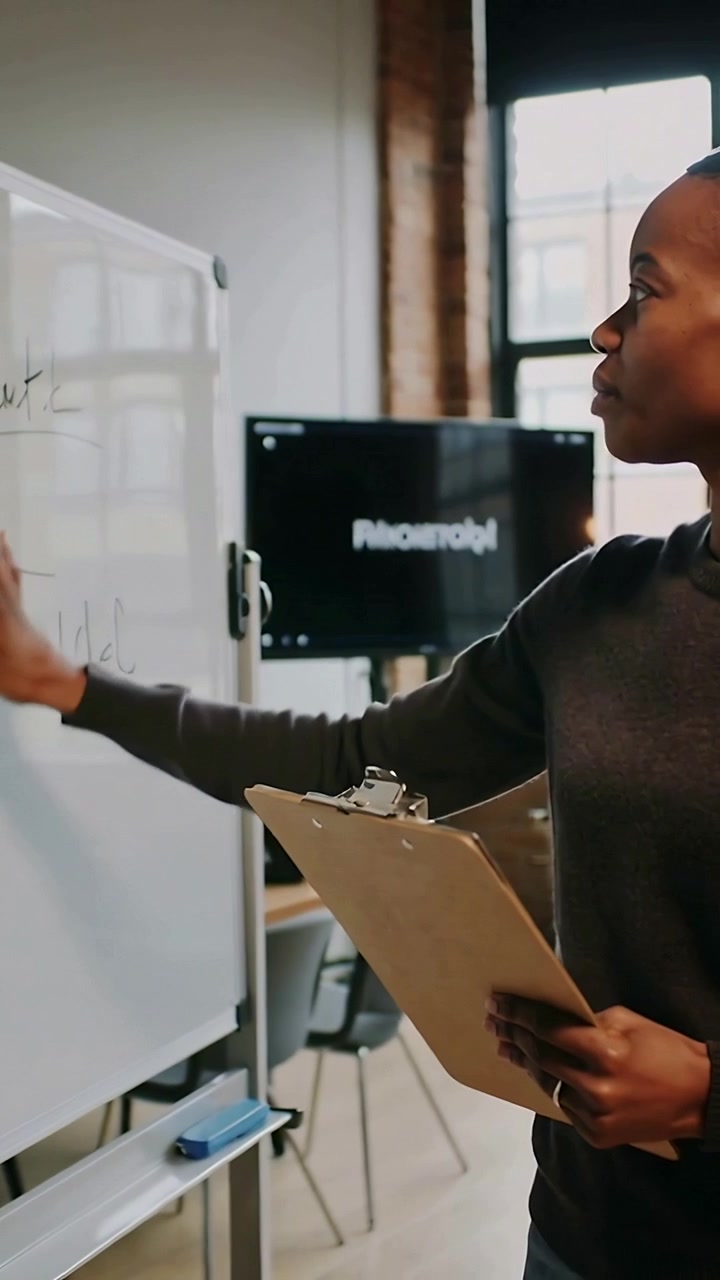 Vertical video: Checking clipboard, woman in dark sweater pointing at board in office, copy space