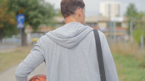 Back-view-of-man-walking-with-a-basketball-and-gym-bag