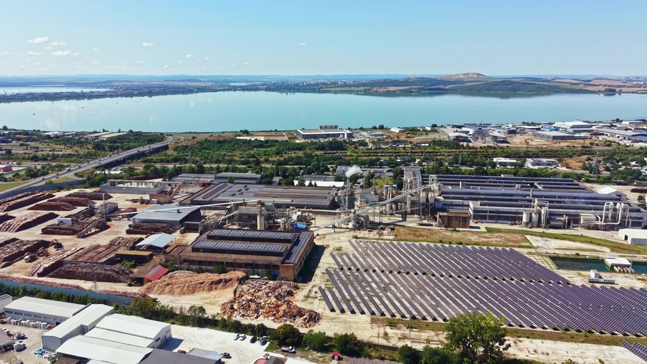 Polígono industrial con paneles solares y cuerpo de agua al fondo durante el día.