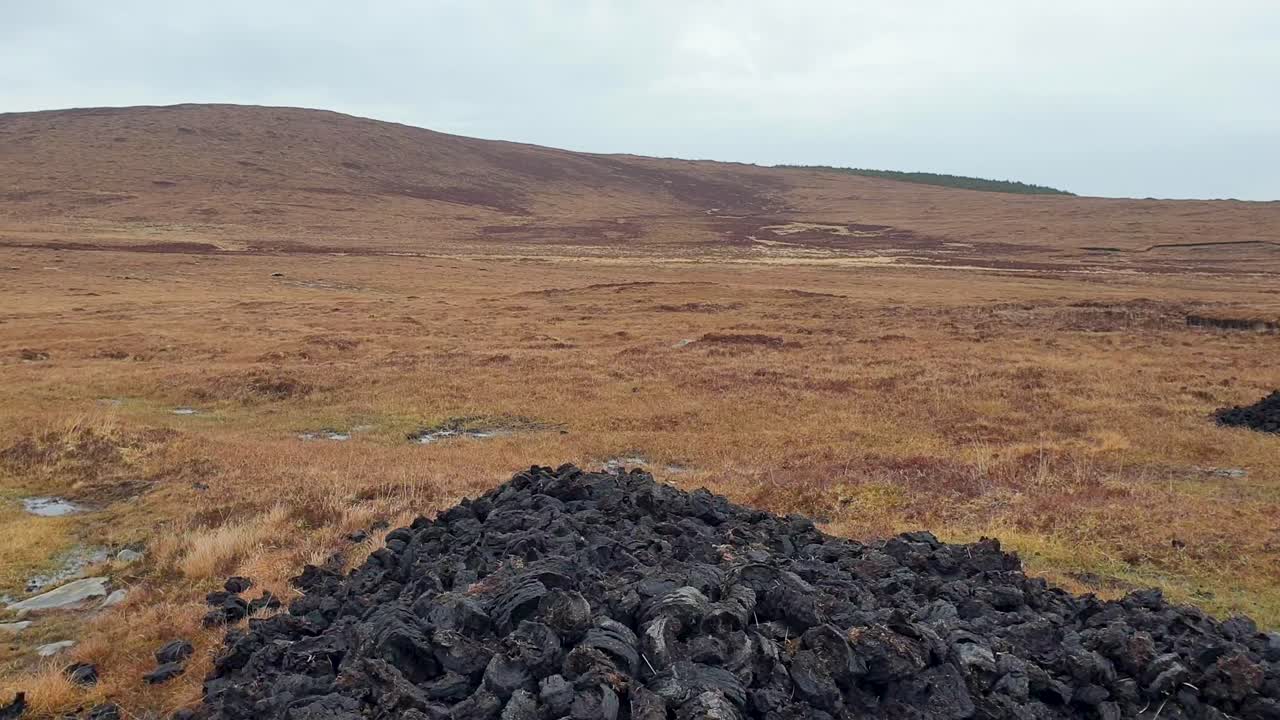 Nærbillede af tørveblokke i en bunke blandt tørt, gyldenbrunt græs og tuegræs på Ydre Hebrider i Skotland, Storbritannien