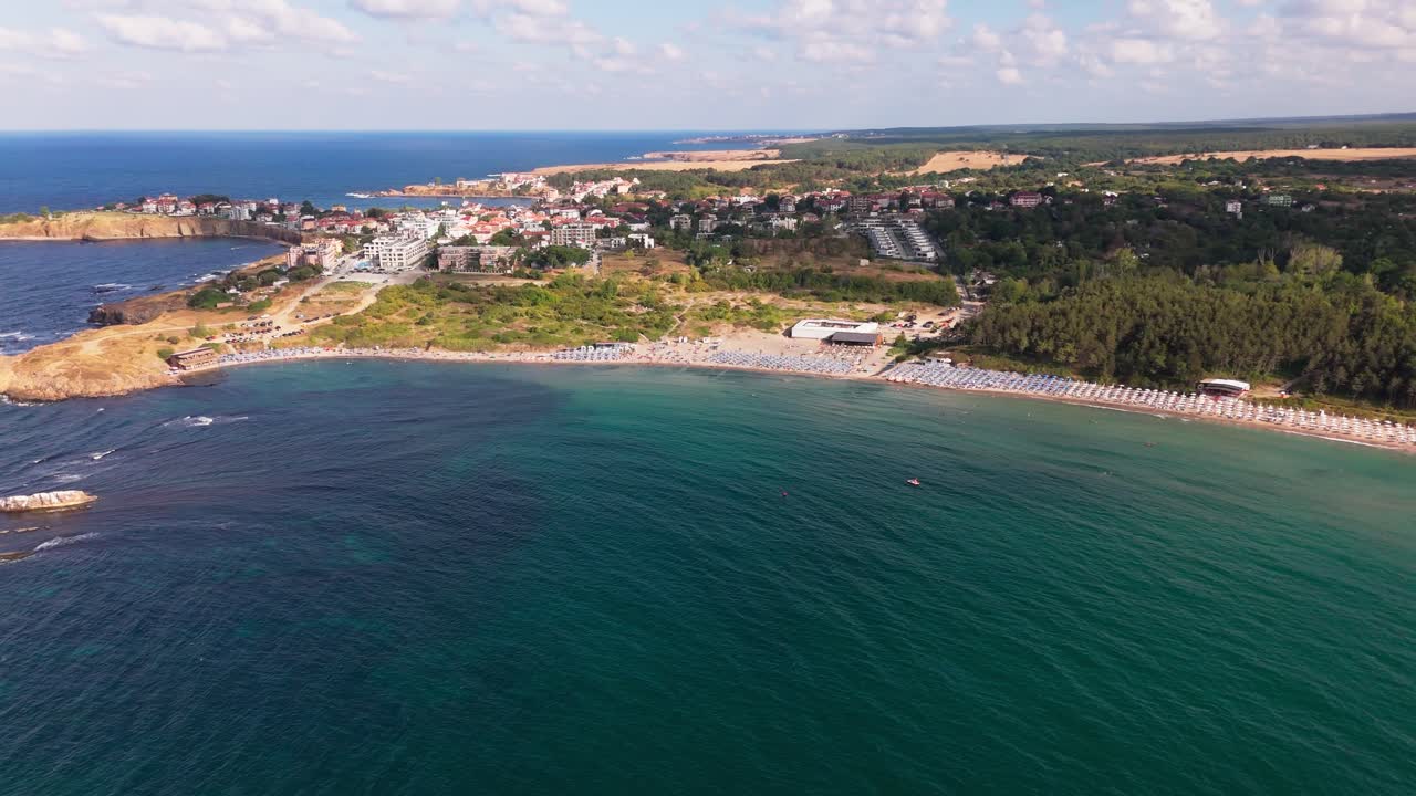 Drone pans left to right across Ahtopol beach, revealing the full coastline, sunbathers, and mainland in a wide scenic aerial view