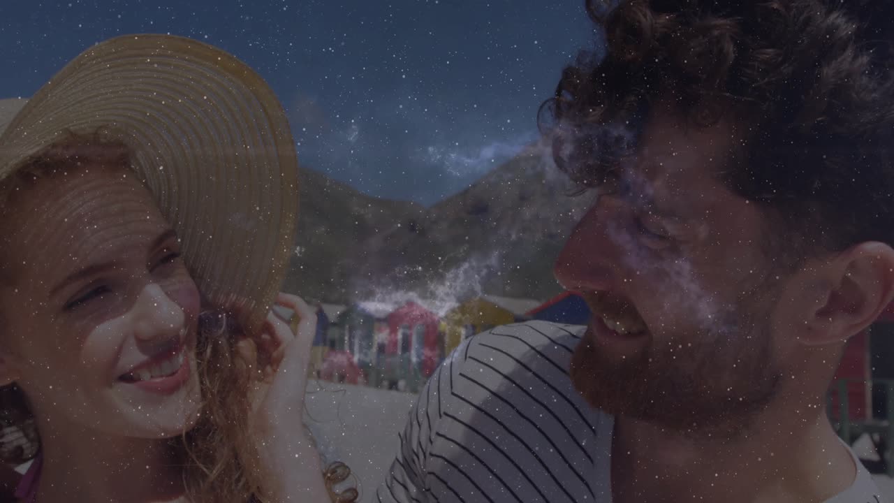 Par med stråhat står på stranden og ser et lens flare, der afslører et stjernefelt-overlay til rejse